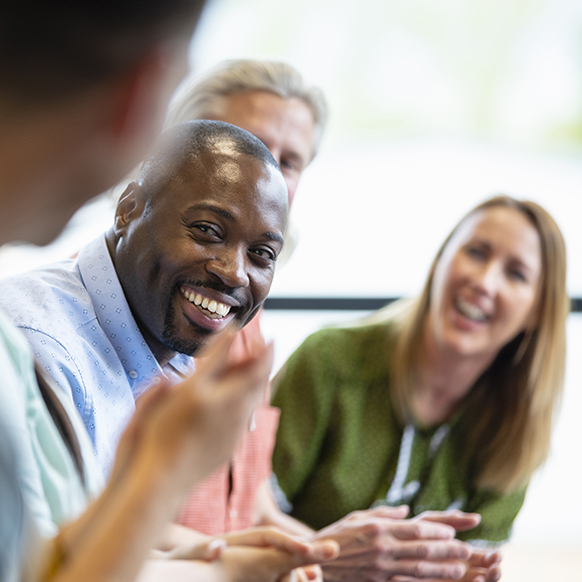Professionals around a conference table looking and smiling at another coworker