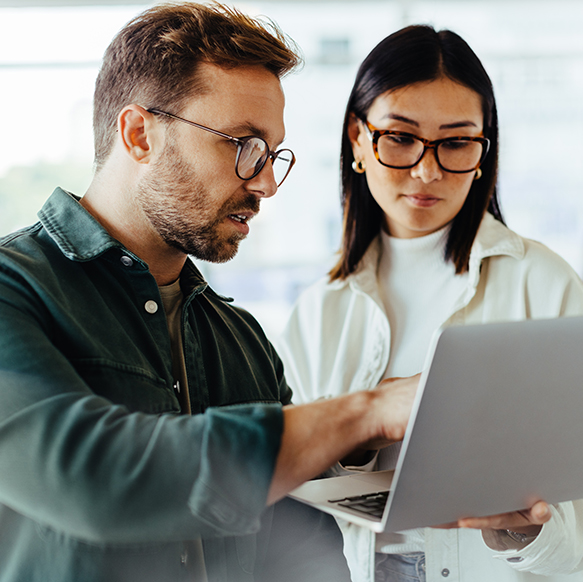 Professional man and woman standing in office reviewing something together on the laptop