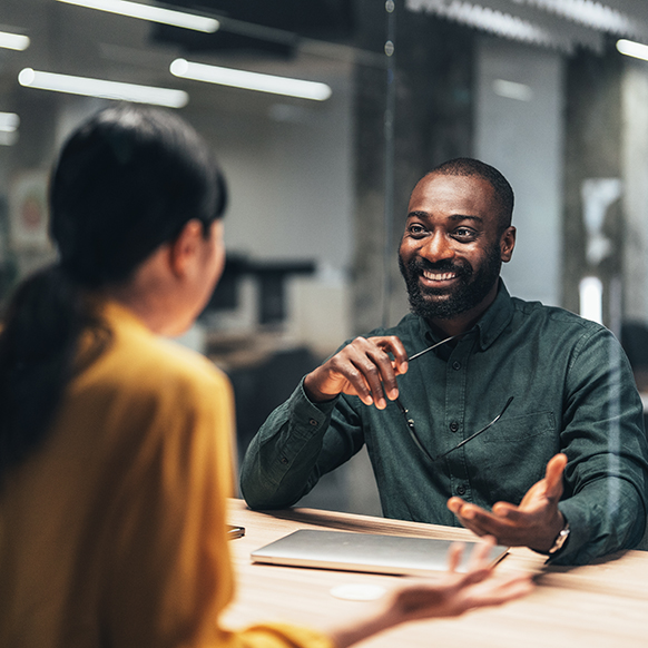 African American professional smiling and sitting across from woman at office desk in the middle of a discussion