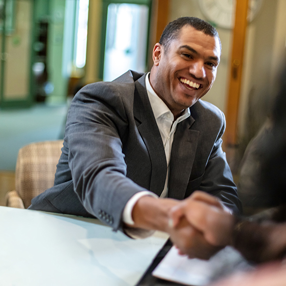 Hispanic businessman shaking hands with another person in an office and sitting behind a desk
