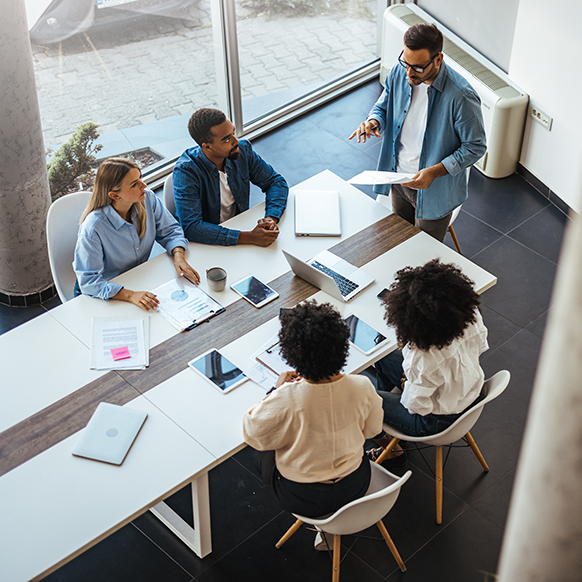 Aerial view looking down at an insurance team around conference table, all seated except man at end of table