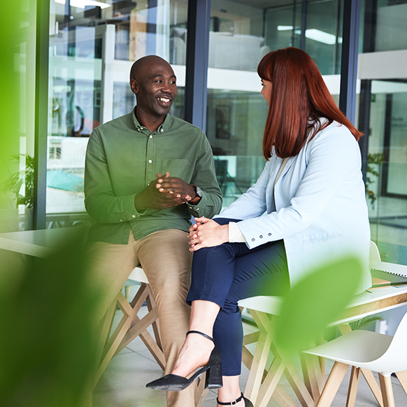 A professional African American man and businesswoman seated in an office environment and chatting