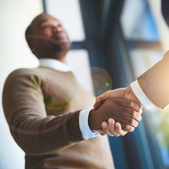 An upward, close up view of a businessman shaking another businessman's hand in an office setting