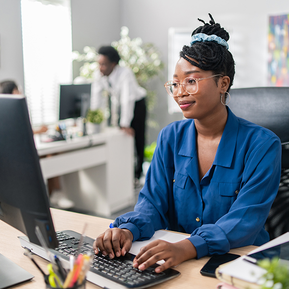 African American woman at her desk typing on her computer with other coworkers at a distance