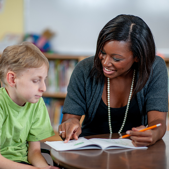 African American teacher helping special needs young boy in classroom setting