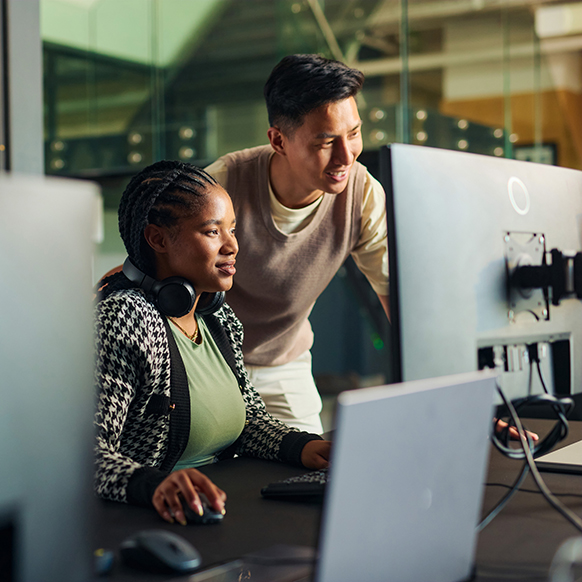 IT Asian man looking at a female African American colleague's computer screen offering technical support
