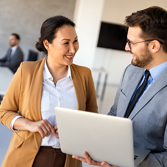 A professional man and women standing in office discussing what is on the laptop of the male's screen 