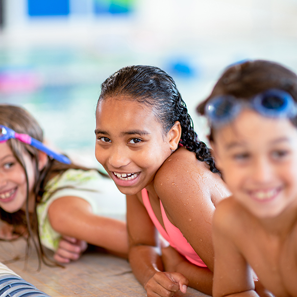 Young kids on edge of swimming pool at YMCA smiling and taking break during class