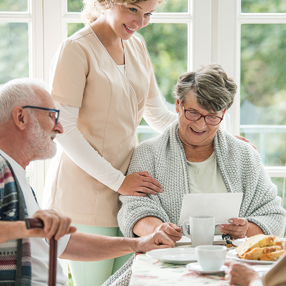 Senior care facility with young caregiver looking over elderly man and woman at table choosing breakfast options